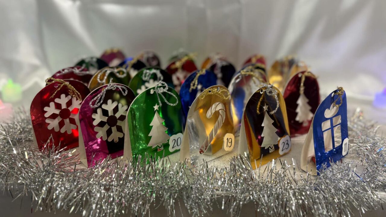 Calendrier de l'Avent d'arches en papier métallisé coloré, ornées de flocons, de sapins, de cannes en sucre et de cadeaux, sur une couronne de guirlande argentée.