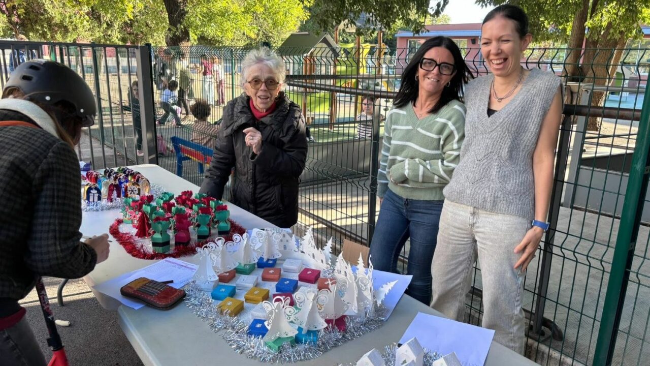 Trois bénévoles de l'APEL souriantes derrière une table de vente de calendriers de l'Avent, dans la cour de l'école.